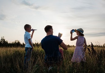 father playing paper aeroplanes with his son & daughter at sunset