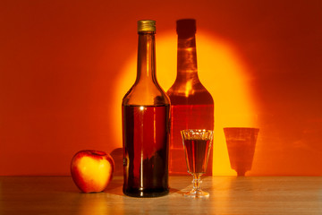 A bottle of French Calvados and a filled glass stand on a table on a yellow-orange background
