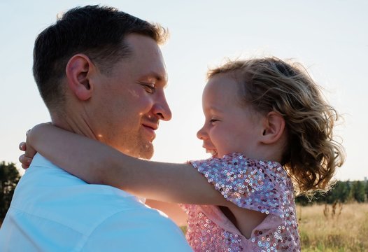 portrait of a father holding his daughter laughing at sunset
