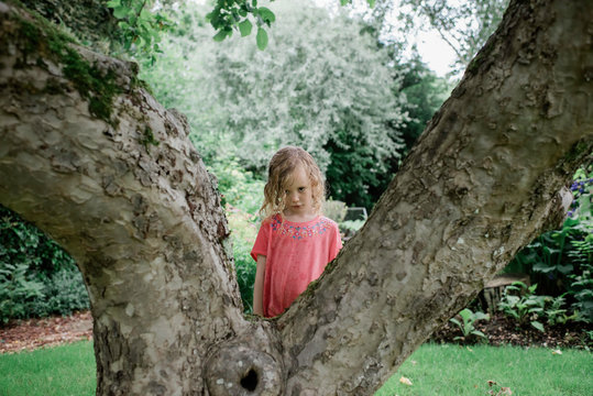 young girl looking sad stood behind a tree in the rain in summer