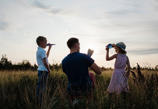 father playing paper aeroplanes with his son & daughter at sunset