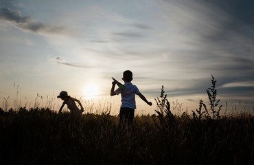 silhouette of siblings playing with paper planes outside at sunset