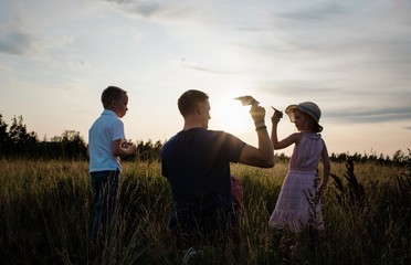 father playing with paper aeroplanes with son and daughter at sunset