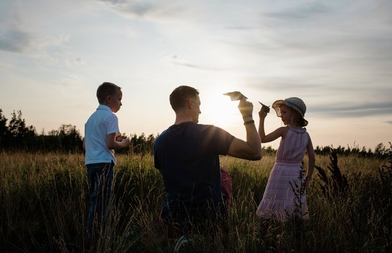 father playing with paper aeroplanes with son and daughter at sunset