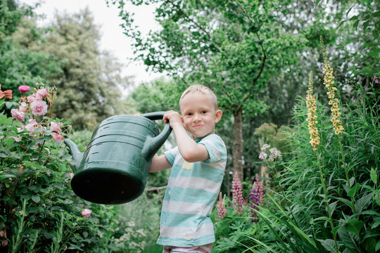 portrait of a young blonde boy watering his english country garden