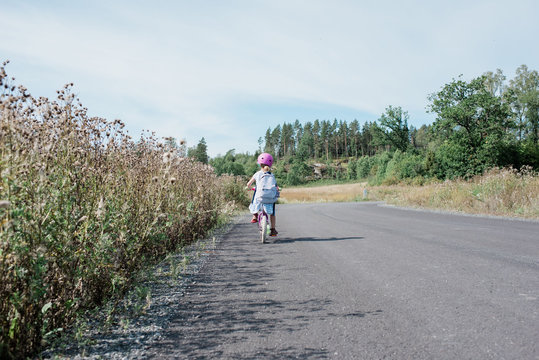 rear view of a young girl cycling home from school along country road