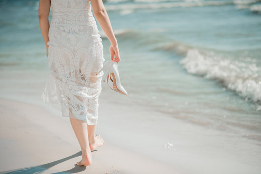 Beautiful bride in luxury wedding dress with bouquet at the sea side. Wedding by the sea. Bride walking around the sea near the place of the wedding ceremony. Back view