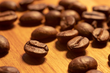 Coffee beans laying on a wooden cutting board in harsh light close up