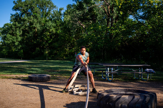 A man pulls a heavy tire with a rope in an outdoor obstacle course - Powered by Adobe