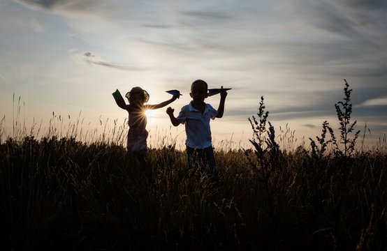 siblings playing outside in a meadow at sunset in summer