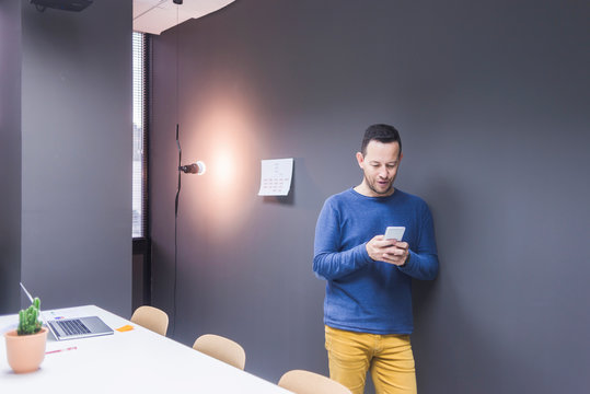 Businessman standing at concrete wall looking at cell phone
