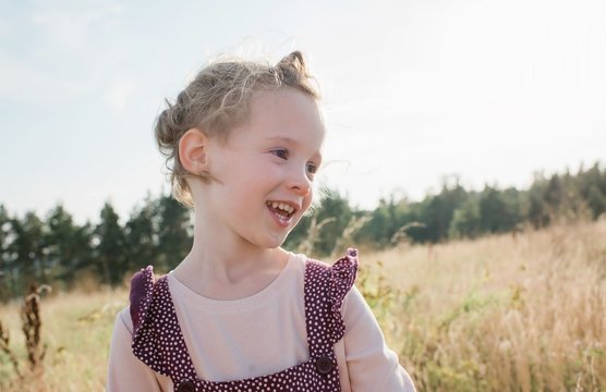 portrait of a young girl smiling walking through a meadow at sunset
