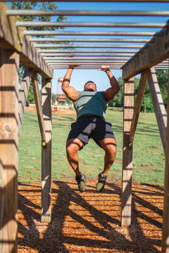 Front view of a strong man swinging across bars in park