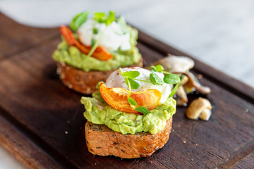 Healthy breakfast, two avocado toasts with poached eggs and mushrooms on the side