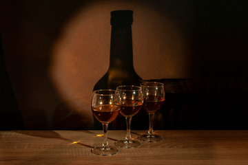 Three glasses with calvados stand on the table against the background of the bottle