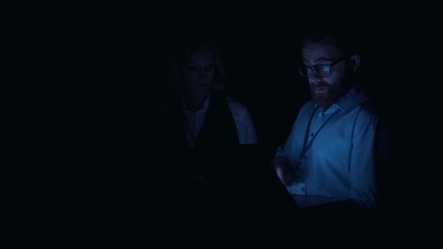 Professional data center team cooperating at computer security. Bearded IT specialist typing on laptop deactivating server room with power failure running away. Blackout.