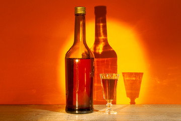 A bottle of French Calvados and a filled glass stand on a table on a yellow-orange background