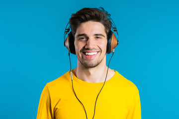Handsome man with headphones dancing isolated on blue background. Party, music, lifestyle, radio and disco concept.