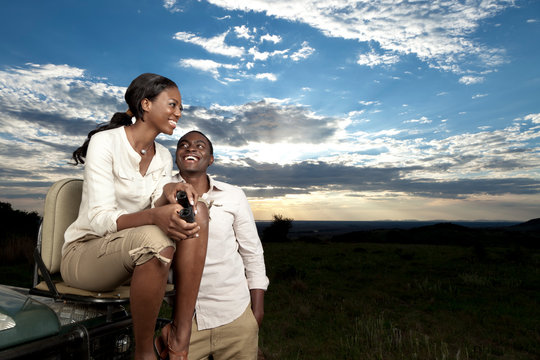 An African couple chatting next to a game viewing vehicle during sunset