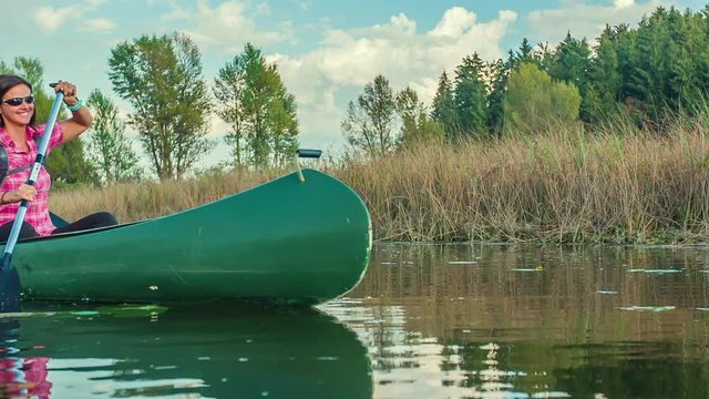 Both people are smiling when they're riding a canoe. Both of them are also paddling a canoe.