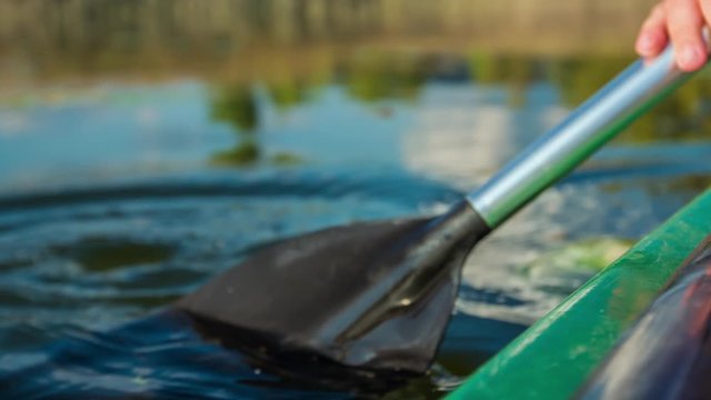 The movement of a paddle during a canoe ride. There are also green leaves swimming on the surface of a lake.