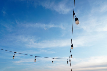 garland of large bulbs on the terrace for decoration on holidays or at night against a blue sky background with small white clouds. decor, creating comfort in a cafe or restaurant, at home