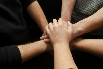 Team spirit, team work. People keeping hands together on black background. Friends.