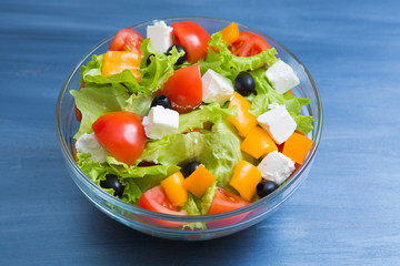 Greek salad in glass bowl on dark gray wooden or metal table