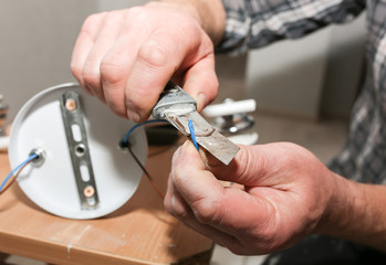 Fototapeta premium Man is holding pliers in his hands. Lamp installation. Electrical insulator for light bulb. Restoration indoors.