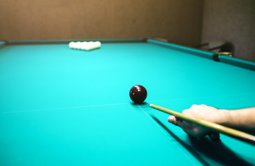 Man is playing billiard. Guy is holding pool cue in his hand. Small black cue ball is on the centre of the green table. Sports and indoor games free time concept.