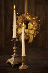 Fototapeta premium two candles in candlesticks on background Christmas wreath on dark wooden background