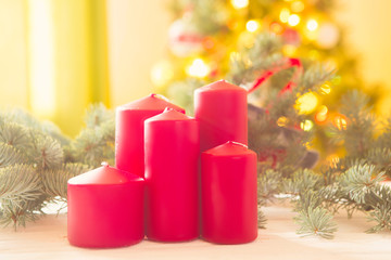 Red christmas candles on white wooden plank against christmas tree in living room