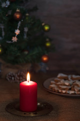 Obraz na płótnie Canvas Christmas candle and in the background Cinnamon star cookies on a plate surrounded by Christmas ornaments on a Sackcloth tablecloth side view .
