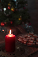 Christmas candle  and in the background Cinnamon star cookies on a plate surrounded by Christmas ornaments on a  Sackcloth tablecloth side view .