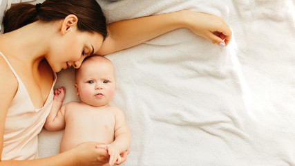 Young beautiful mother lies with the baby on the bed, gently kisses, sleeping together.