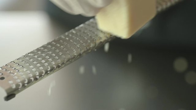 Slow motion close up of hand in glove grating parmesan cheese from high angle.