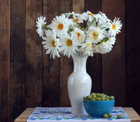 white daisies and dahlias in a vase and gooseberries.