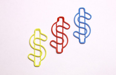 Three multi-colored figures of the dollar. Curly stationery colored paper clips. The view from the top