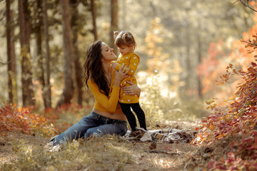Beautiful young mother and her happy daughter are having fun in the forest in sunset. They are holding hands and laughing.