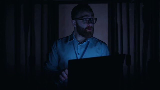 Caucasian IT engineer working on laptop turning off digital server room typing keyboard in panic trying to solve problem. Data center blackout. Power failure.