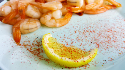 Boiled peeled shrimp on a blue plate close-up. Shrimp with lemon and pepper.