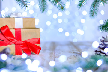 Christmas bokeh background with fir branches. A gift boxs on the table with red ribbon. Copy space, soft focus.
