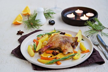 Roasted duck leg with potatoes, carrots and slices of orange on a ceramic plate on a light concrete background. Christmas and New Year dishes recipes. Duck recipes. French cuisine