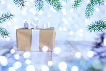 Christmas bokeh background with fir branches. A gift box on the table with white ribbon. Copy space, soft focus.