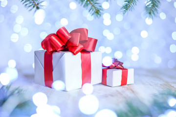 Christmas bokeh background with fir branches. A wite gift boxs on the table with red ribbon. Copy space, soft focus.