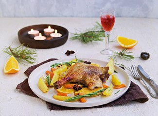 Roasted duck leg with potatoes, carrots and slices of orange on a ceramic plate on a light concrete background. Christmas and New Year dishes recipes. Duck recipes. French cuisine