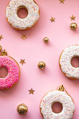 Christmas toys in the form of donuts on a pink background with gold decor. Creative food minimalism, top view with copy space