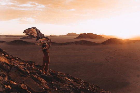 A sunset in Namibian desert and a girl with a scarf standing