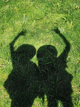 Shadow of two women on green grass waving hello