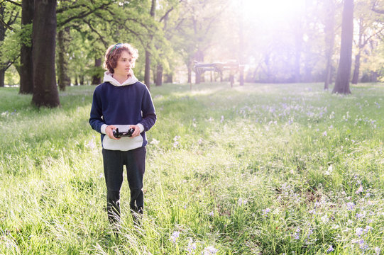 Teenage boy standing next to a flying drone in park in spring